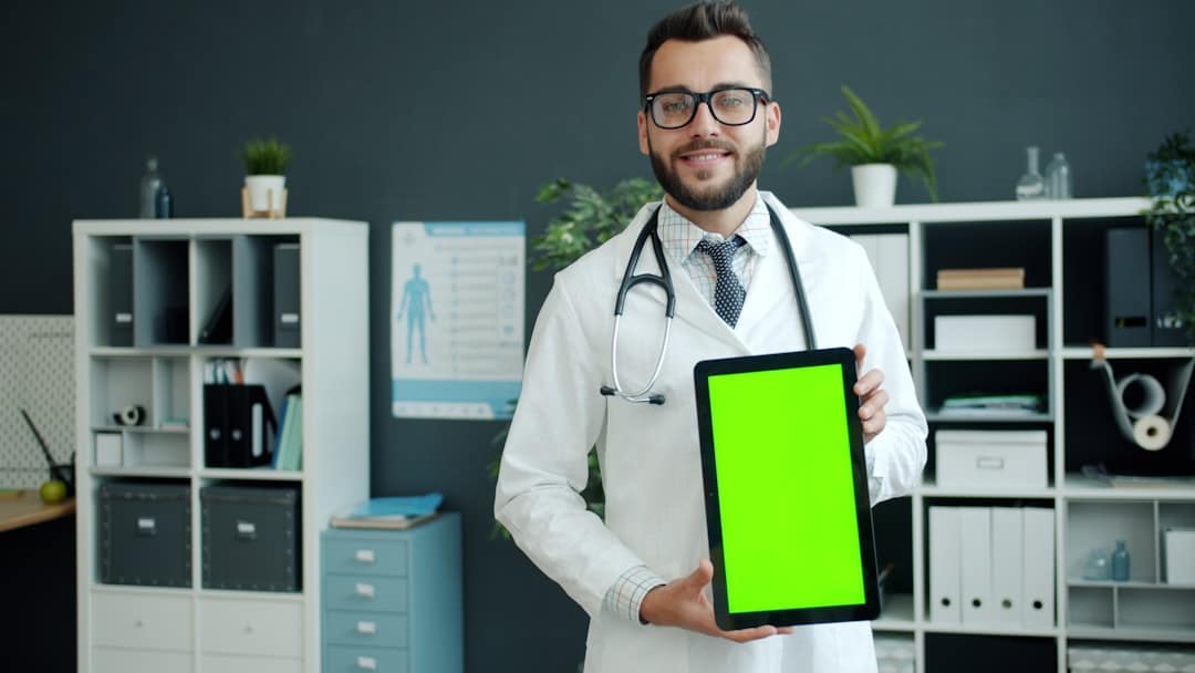 A well-dressed real estate agent smiles while using a tablet inside a bright, modern brokerage office, showcasing the benefits of a tech-forward environment.
