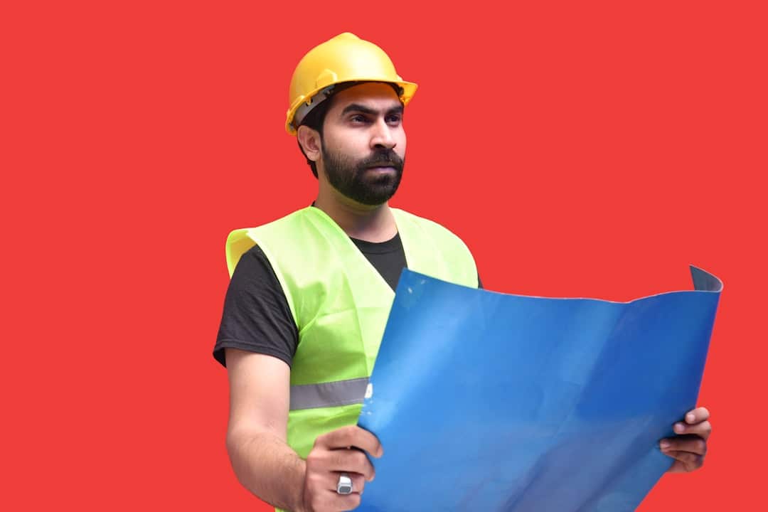 Focused professional architect in a modern office meticulously examining a complex architectural blueprint, symbolizing di...